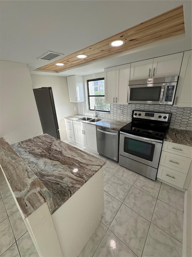 kitchen with sink, stainless steel appliances, tasteful backsplash, dark stone counters, and white cabinets