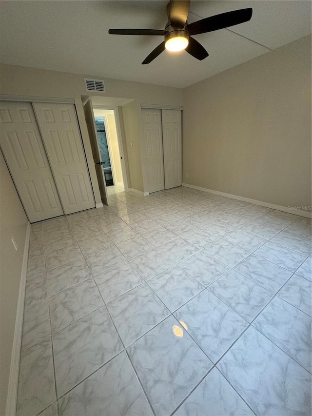 unfurnished bedroom with ceiling fan and multiple closets