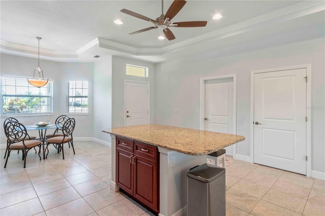 kitchen featuring ornamental molding, a raised ceiling, ceiling fan, pendant lighting, and a center island