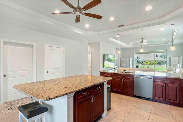 kitchen featuring a tray ceiling, sink, dishwasher, a kitchen island, and a breakfast bar area