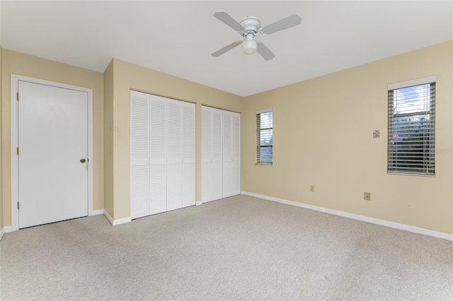 unfurnished bedroom featuring ceiling fan, two closets, light carpet, and multiple windows