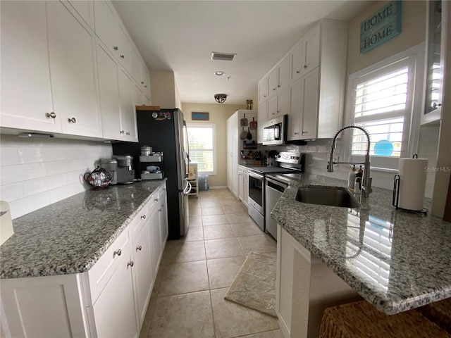 kitchen featuring tasteful backsplash, light tile floors, sink, white cabinets, and appliances with stainless steel finishes