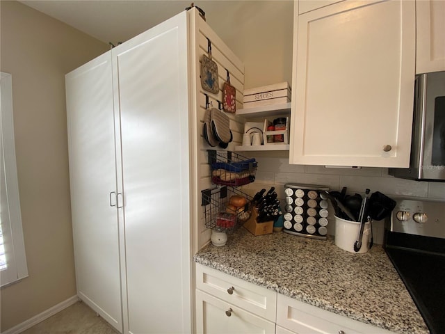 kitchen with light stone countertops, range, backsplash, and white cabinetry