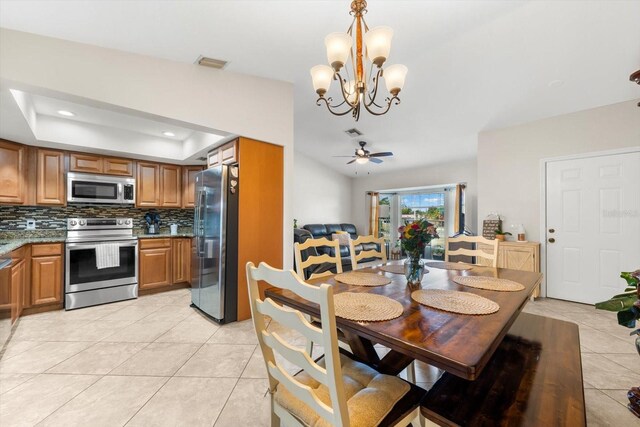 dining space featuring ceiling fan with notable chandelier, a raised ceiling, and light tile patterned floors