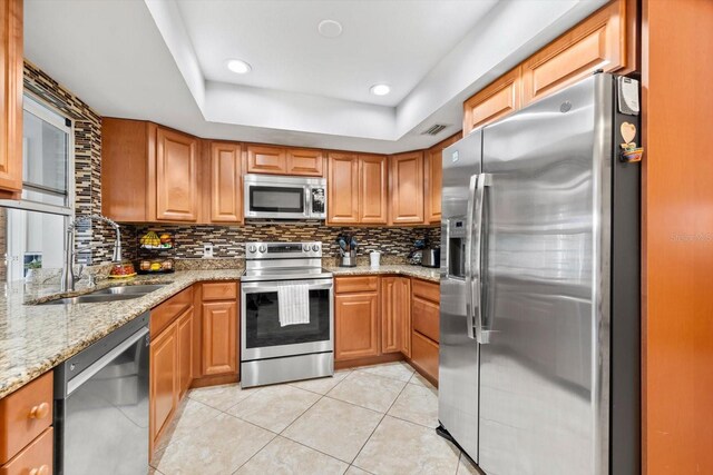 kitchen with sink, light stone countertops, light tile patterned floors, a tray ceiling, and stainless steel appliances