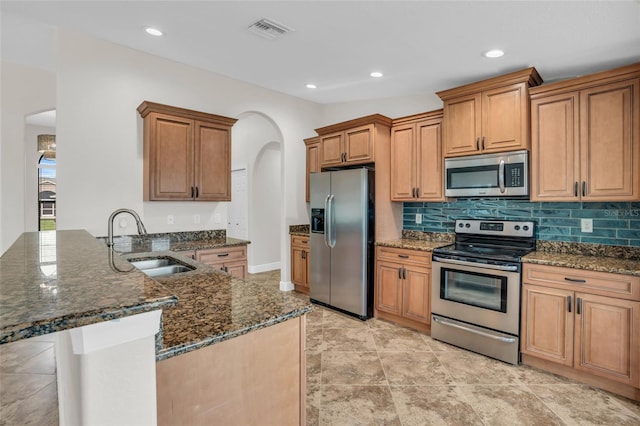 kitchen with sink, stainless steel appliances, kitchen peninsula, dark stone countertops, and decorative backsplash