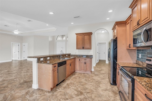 kitchen with kitchen peninsula, a kitchen bar, dark stone counters, stainless steel appliances, and ceiling fan