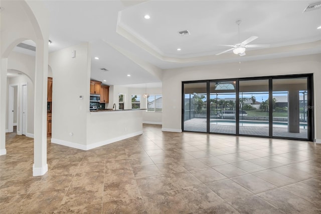 unfurnished living room featuring a raised ceiling and ceiling fan