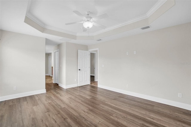 empty room featuring wood-type flooring, a tray ceiling, and crown molding