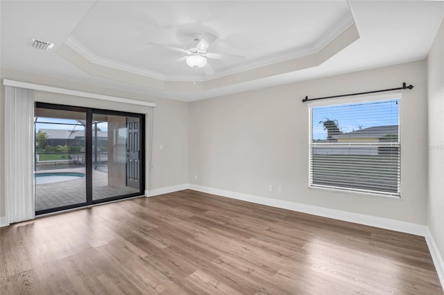 empty room with hardwood / wood-style flooring, a raised ceiling, and a healthy amount of sunlight