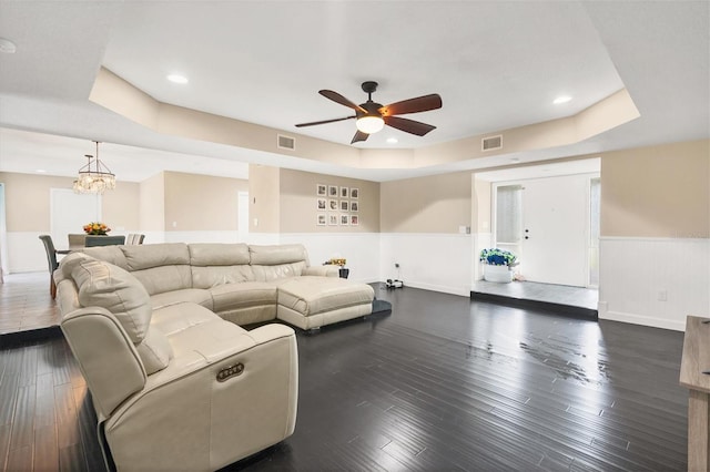 living room with dark wood-type flooring, a tray ceiling, and ceiling fan with notable chandelier