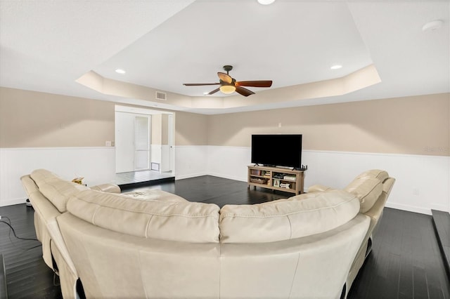 living room featuring dark hardwood / wood-style flooring, a raised ceiling, and ceiling fan