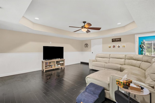 living room with ceiling fan, dark hardwood / wood-style flooring, and a raised ceiling