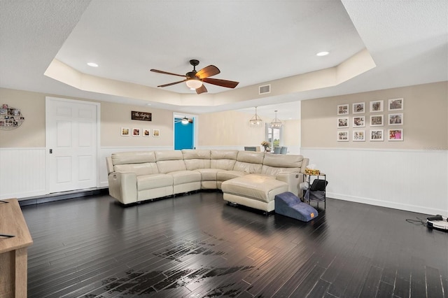 living room featuring dark wood-type flooring, ceiling fan, and a tray ceiling