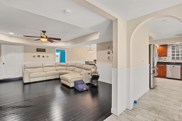 living room featuring a tray ceiling, ceiling fan, and light hardwood / wood-style flooring