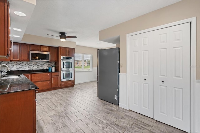 kitchen featuring sink, light hardwood / wood-style flooring, ceiling fan, stainless steel appliances, and decorative backsplash