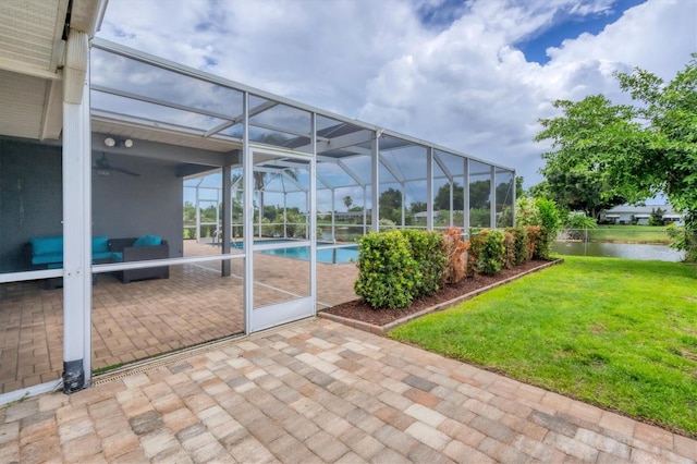 view of patio featuring a water view, ceiling fan, and glass enclosure