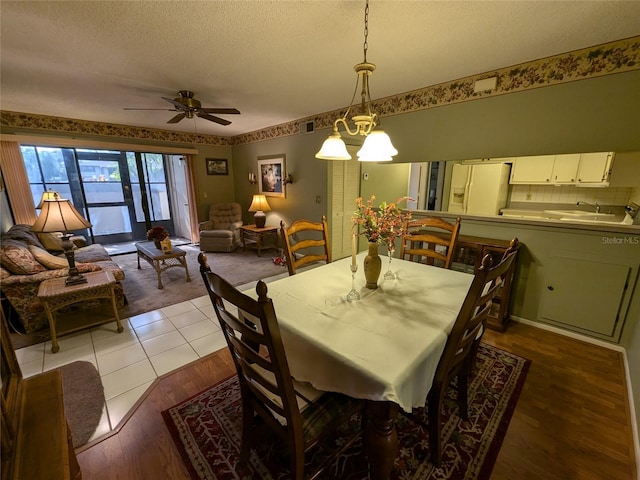 dining space featuring sink, ceiling fan with notable chandelier, light hardwood / wood-style floors, and a textured ceiling