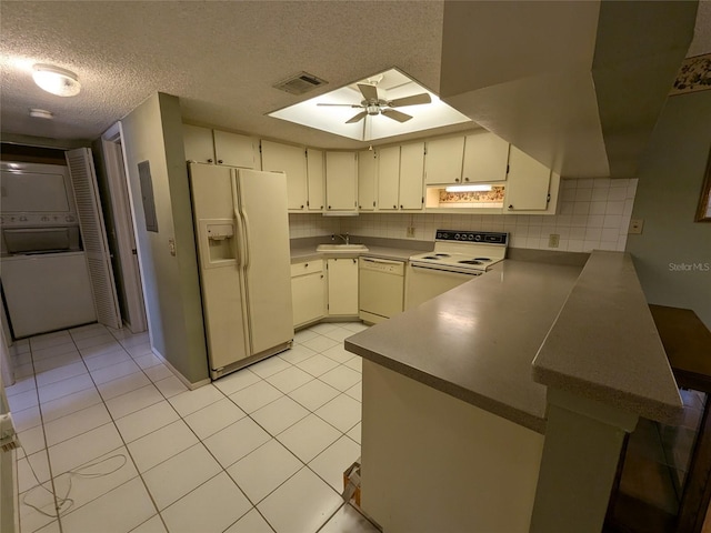 kitchen featuring light tile patterned flooring, white appliances, stacked washer / drying machine, and kitchen peninsula