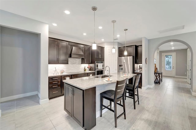 kitchen with dark brown cabinets, an island with sink, stainless steel appliances, and custom exhaust hood