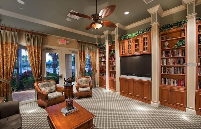 carpeted living room featuring french doors, crown molding, ceiling fan, built in shelves, and ornate columns