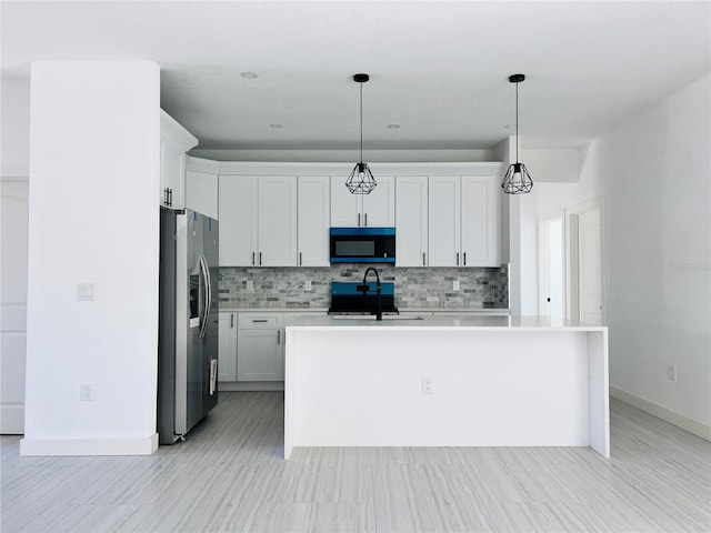 kitchen featuring decorative light fixtures, a kitchen island with sink, white cabinets, and stainless steel fridge