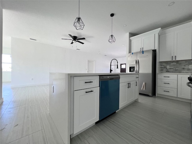 kitchen featuring a kitchen island with sink, stainless steel appliances, ceiling fan, decorative backsplash, and white cabinets