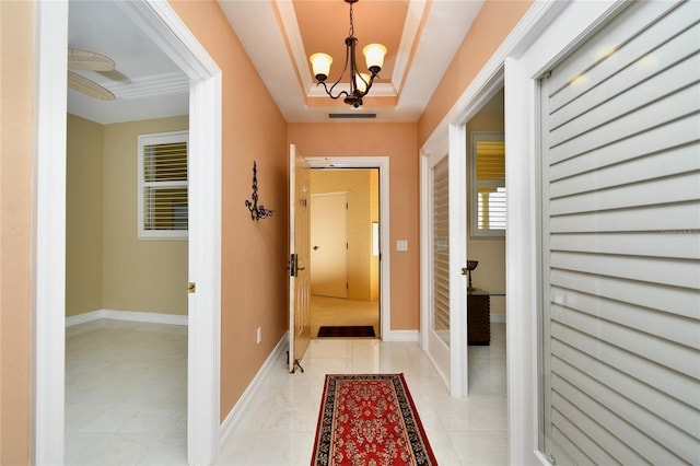 doorway featuring crown molding, a tray ceiling, and a chandelier