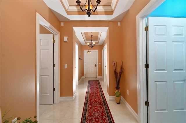 corridor featuring ornamental molding, a raised ceiling, and a chandelier