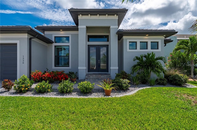 entrance to property featuring a garage, a yard, and french doors