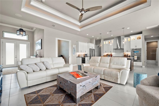 living room featuring french doors, ornamental molding, a tray ceiling, ceiling fan, and a high ceiling