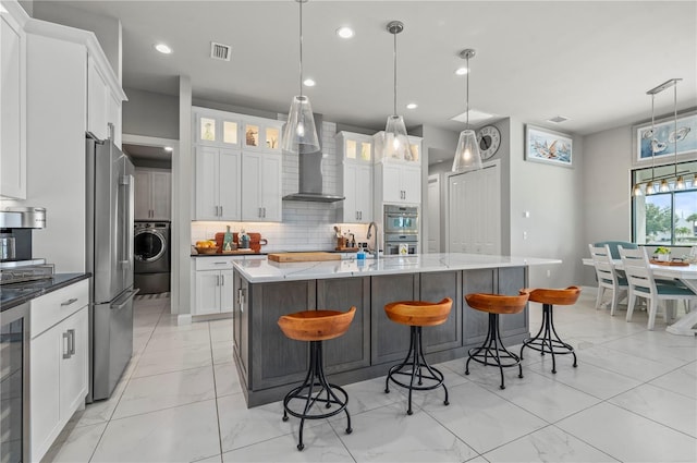 kitchen with pendant lighting, white cabinetry, washer / clothes dryer, and wall chimney range hood