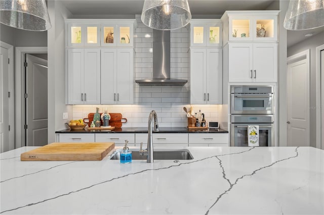 kitchen featuring hanging light fixtures, wall chimney range hood, backsplash, dark stone countertops, and white cabinets