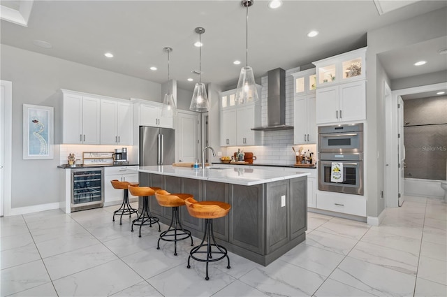 kitchen with a center island with sink, white cabinets, wine cooler, wall chimney exhaust hood, and stainless steel appliances