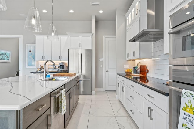 kitchen with pendant lighting, sink, wall chimney exhaust hood, appliances with stainless steel finishes, and white cabinetry