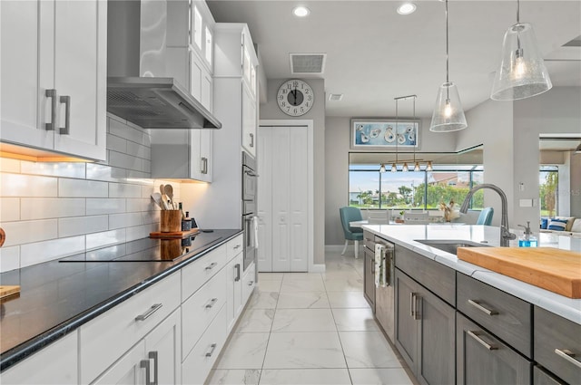 kitchen featuring backsplash, wall chimney exhaust hood, black electric cooktop, pendant lighting, and white cabinetry