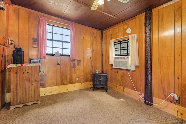 interior space with wood walls, ceiling fan, carpet, and a wood stove