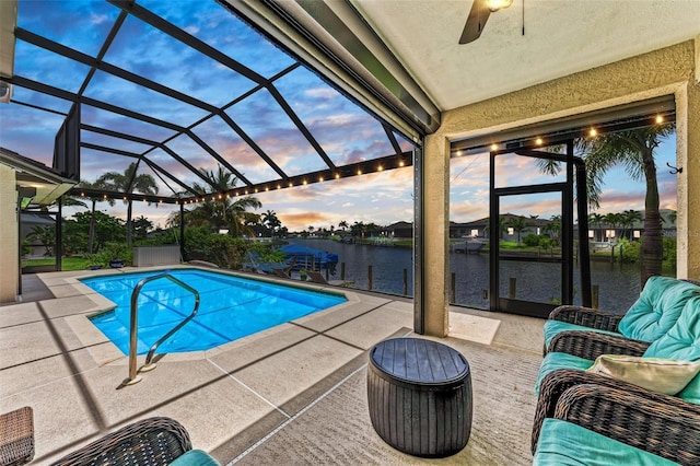 pool at dusk with a dock, a water view, ceiling fan, a lanai, and a patio area