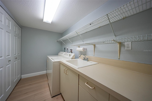 laundry area with cabinets, sink, independent washer and dryer, a textured ceiling, and light hardwood / wood-style floors