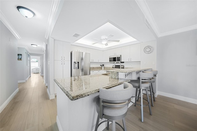 kitchen featuring a kitchen breakfast bar, kitchen peninsula, appliances with stainless steel finishes, light stone counters, and white cabinetry