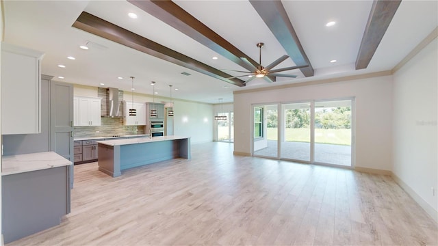 kitchen with light hardwood / wood-style floors, ceiling fan, decorative light fixtures, a kitchen island, and wall chimney exhaust hood