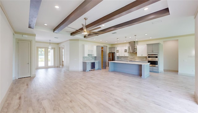 kitchen featuring light hardwood / wood-style floors, hanging light fixtures, wall chimney exhaust hood, and a kitchen island with sink