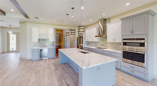 kitchen with pendant lighting, beverage cooler, wall chimney exhaust hood, sink, and a large island