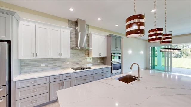 kitchen featuring wall chimney exhaust hood, stainless steel appliances, sink, hanging light fixtures, and light stone counters