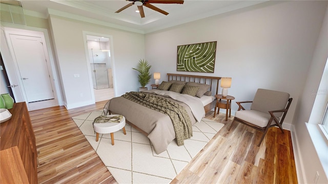 bedroom featuring light wood-type flooring, ceiling fan, a tray ceiling, and ensuite bath