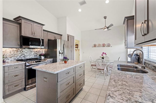 kitchen featuring sink, a center island, stainless steel appliances, light stone counters, and vaulted ceiling