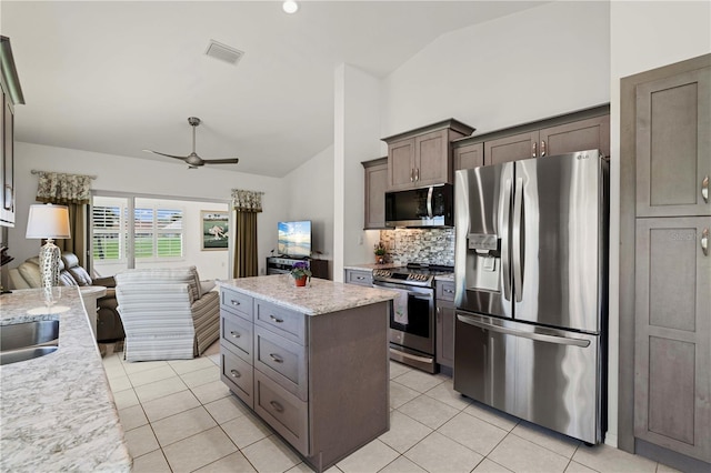 kitchen featuring decorative backsplash, light stone counters, stainless steel appliances, a kitchen island, and lofted ceiling