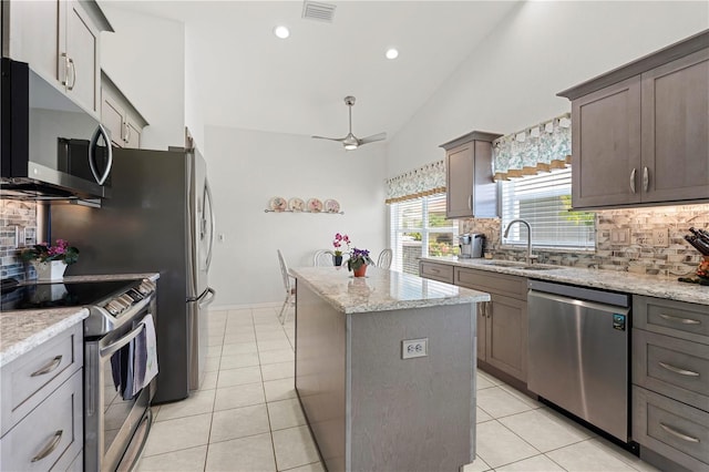 kitchen with light stone countertops, appliances with stainless steel finishes, sink, a center island, and lofted ceiling