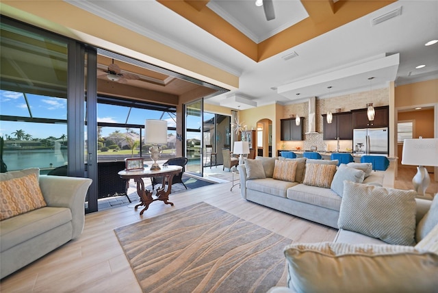 living room with a water view, a raised ceiling, ceiling fan, and ornamental molding