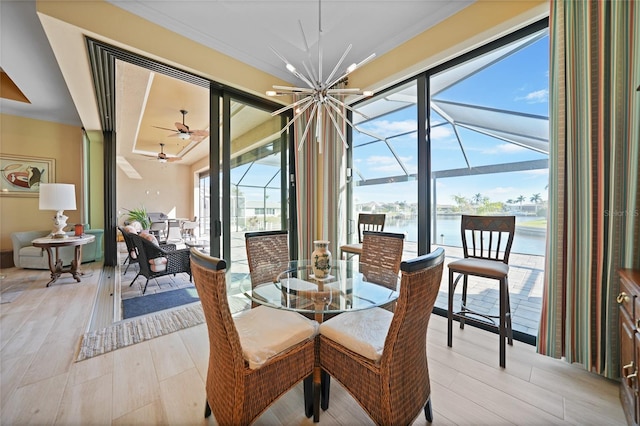 dining space with a wealth of natural light, light hardwood / wood-style flooring, a water view, and ceiling fan with notable chandelier